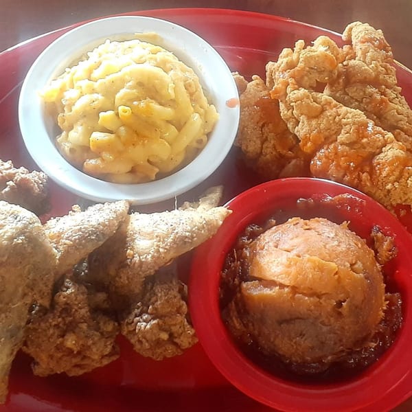 A soul food platter with fried chicken, macaroni and cheese, and candied yams on a red plate.