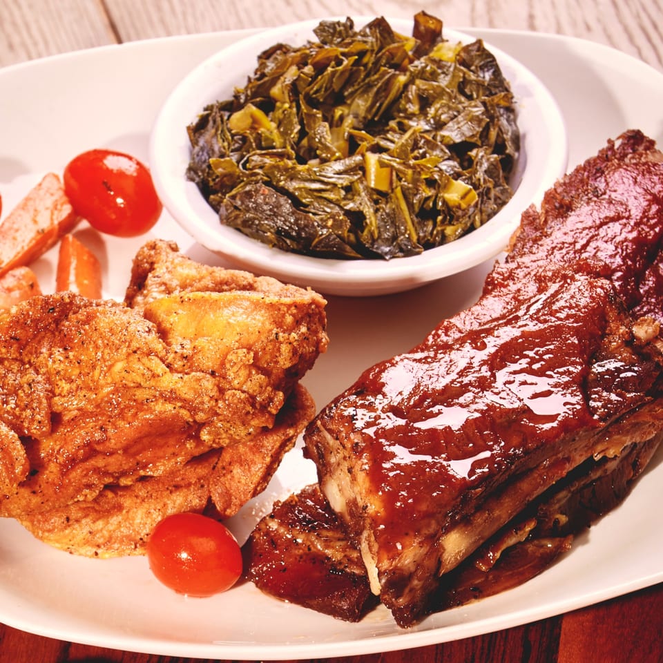 Platter of barbecue ribs, fried chicken, braised greens, bread, and cherry tomatoes.
