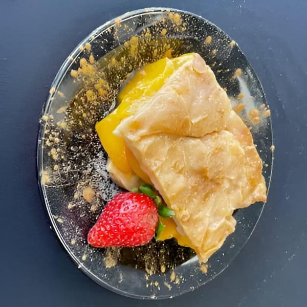 Aunt Berta's Kitchen's peach cobbler with a strawberry garnish on a clear plate.