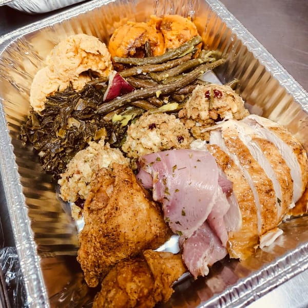 Aunt Berta's Kitchen soul food spread in a foil pan, featuring fried chicken, sliced turkey, and sides.