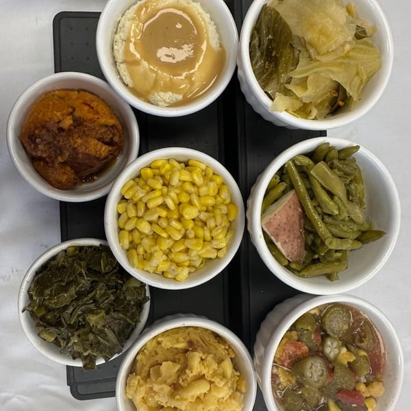 Eight small white bowls filled with various soul food sides, including mashed potatoes, greens, and corn.