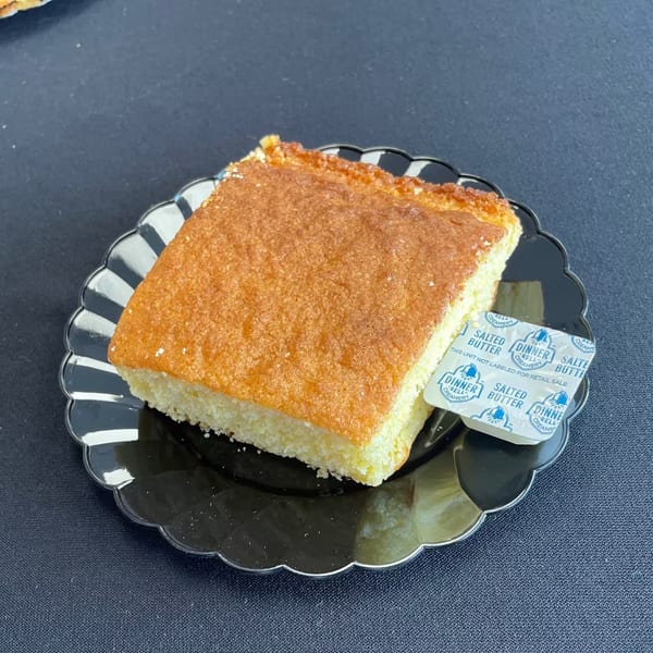 Aunt Berta's Kitchen cornbread slice with two packets of salted butter on a black plate.