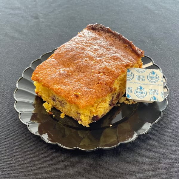 Aunt Berta's Kitchen's cornbread with a side of butter on a black scalloped plate.