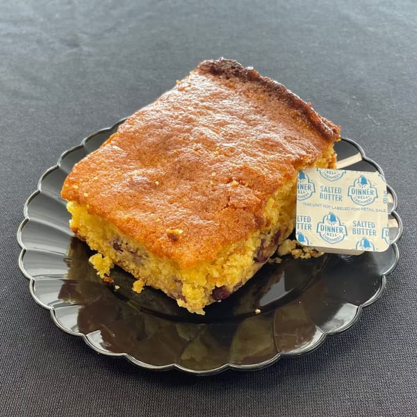 Aunt Berta's Kitchen cornbread with a side of salted butter on a black scalloped plate.