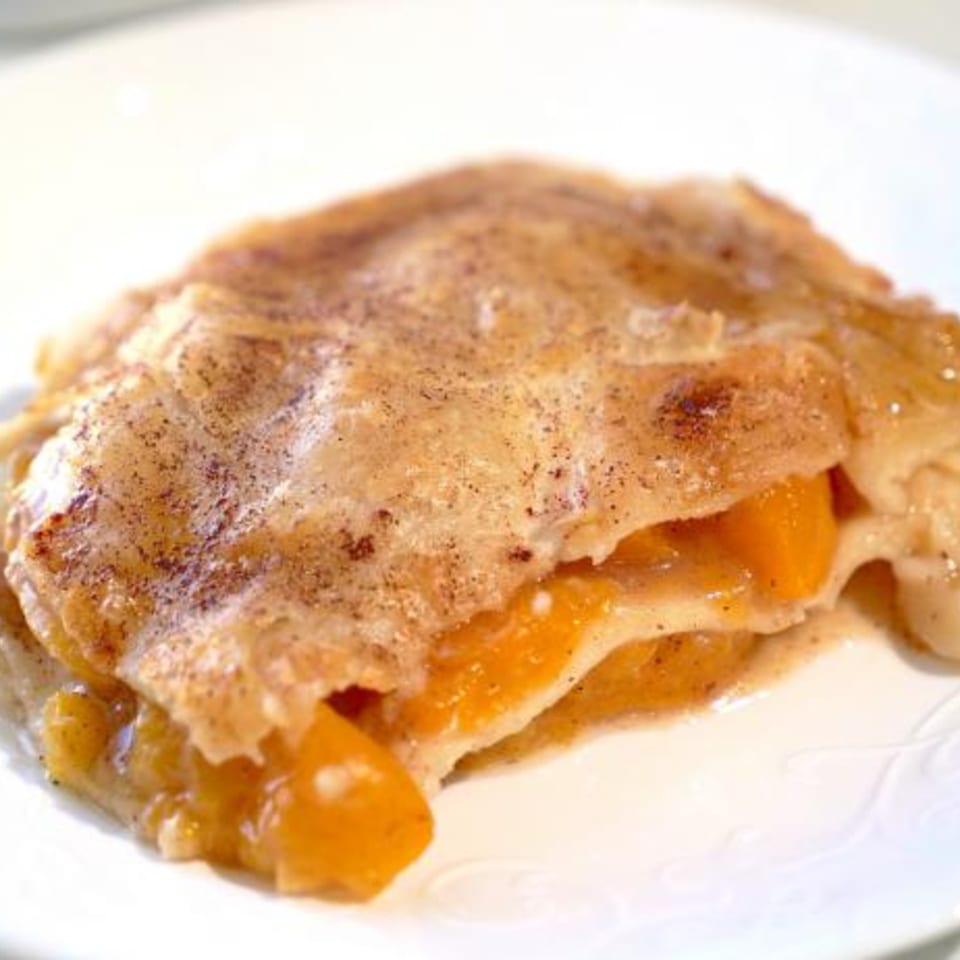 Close-up of a golden, flaky pastry filled with bright orange fruit or jam on a white plate.