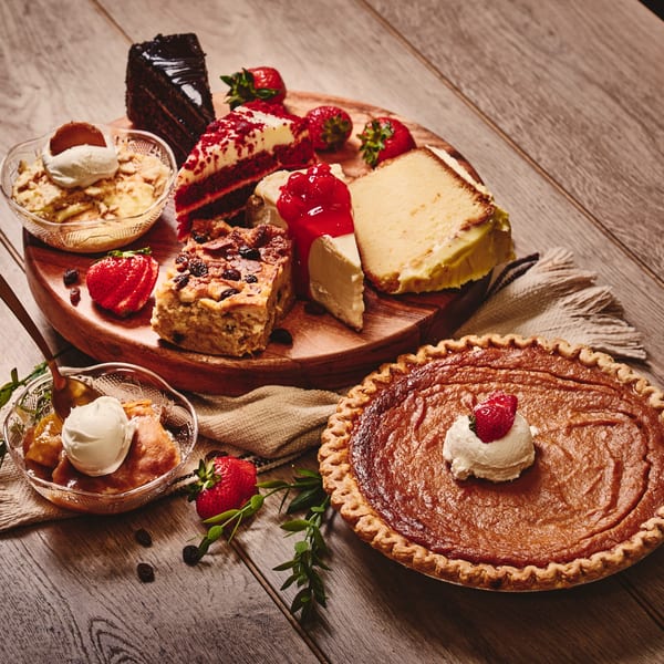 A dessert platter with various cakes, cheesecake, bread pudding, and a sweet potato pie.