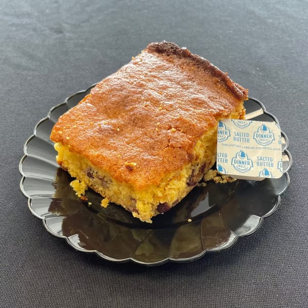 Aunt Berta's Kitchen's cornbread with a side of salted butter on a black scalloped plate.